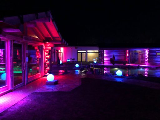 Saunalandschaft Bunte Beleuchtung eines modernen Außenbereichs mit Schwimmbecken bei Nacht.