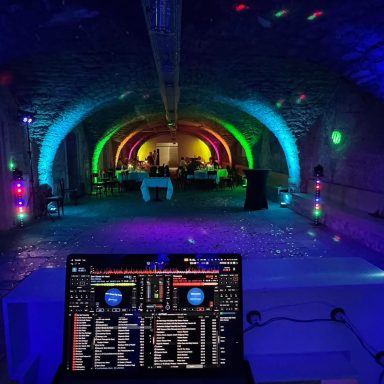 Gewölbekeller DJ-Pult in einem farbenfroh beleuchteten Veranstaltungssaal mit Bögen.